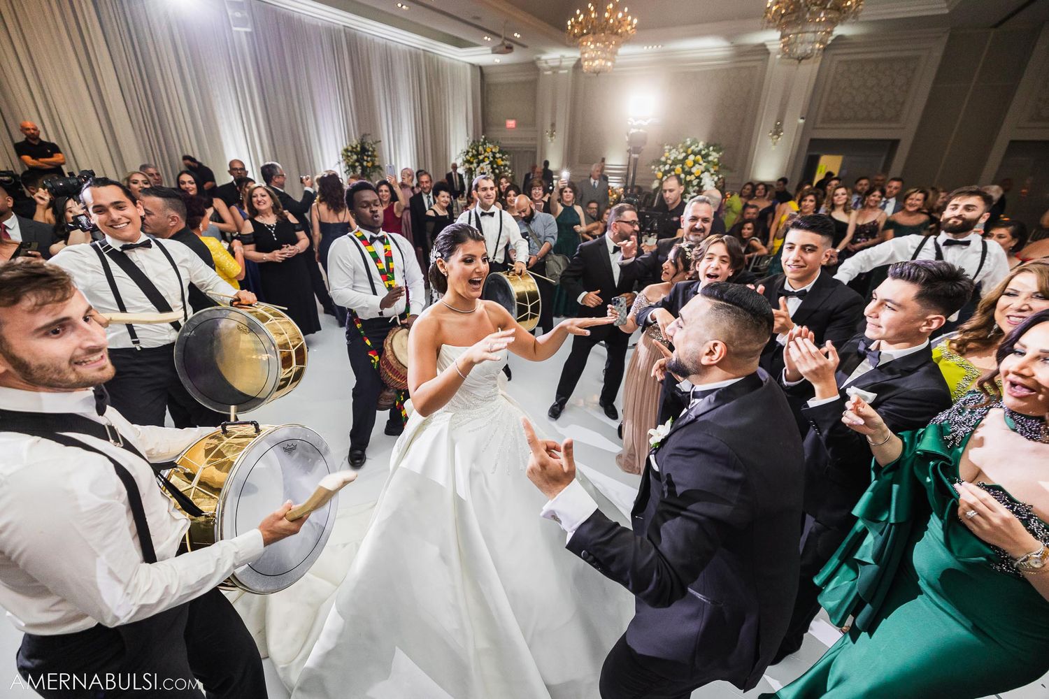 Festive wedding reception with drummers surrounding dancing guests in an elegant ballroom.