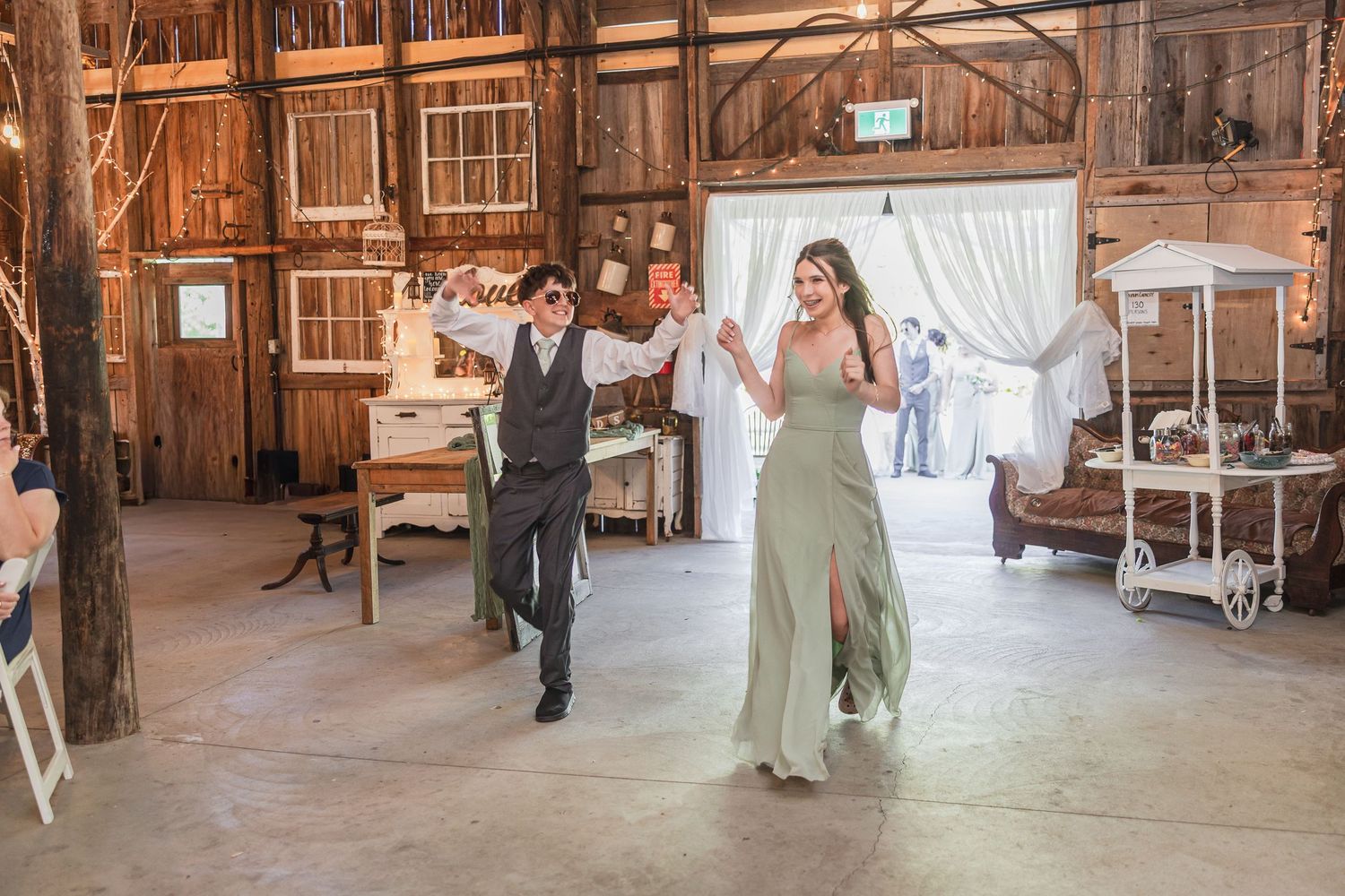 Bride and groomsman make grand entrance into rustic barn wedding reception venue.