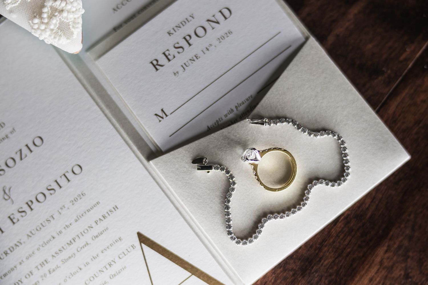 Wedding invitation suite with response card, gold and silver rings, and pearl necklace on elegant white background.
