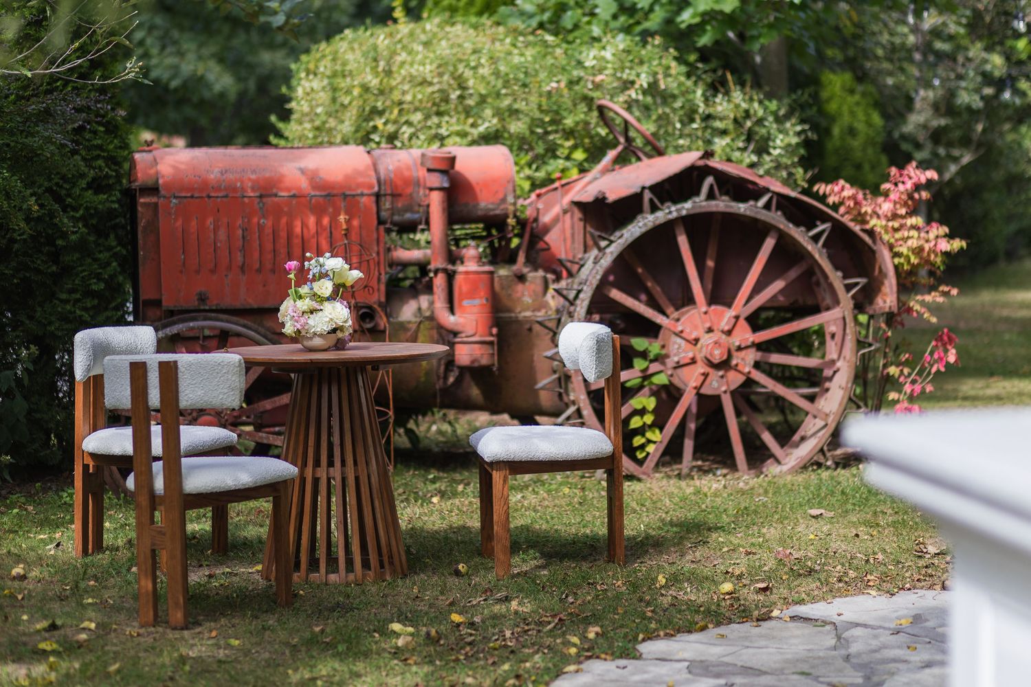 Rustic outdoor wedding seating area with wooden table and chairs beside a vintage red tractor.