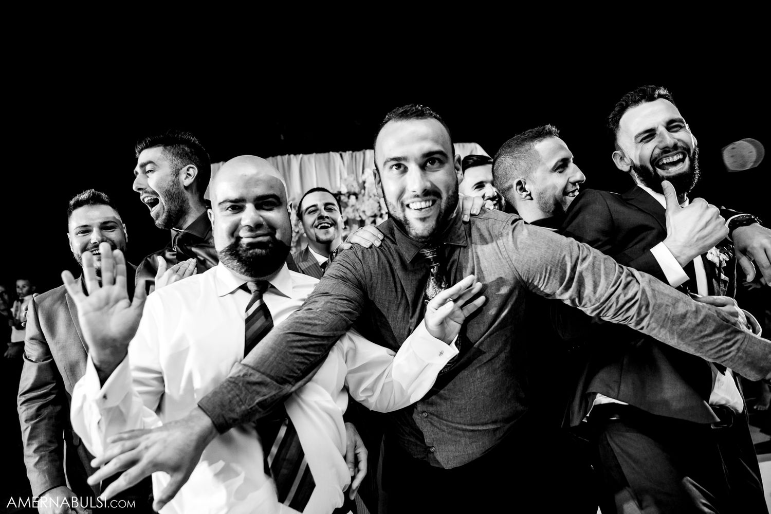 Black and white panorama of wedding guests sharing joyful candid moments during the celebration.