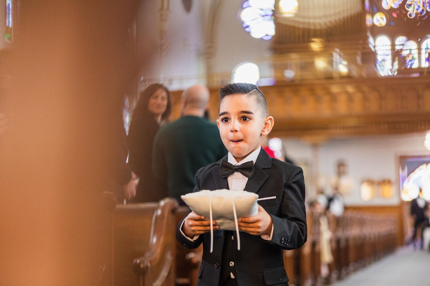 Young attendant in bow tie and formal wear walks church aisle during ceremony.