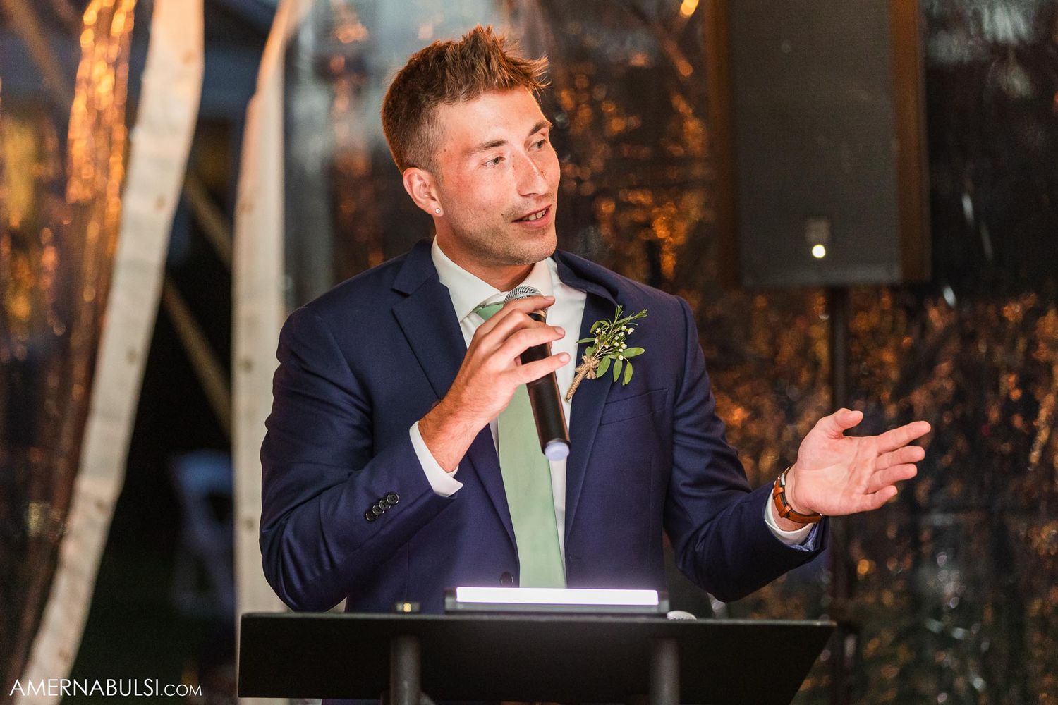 A wedding speech is delivered at an evening reception with rustic decor.