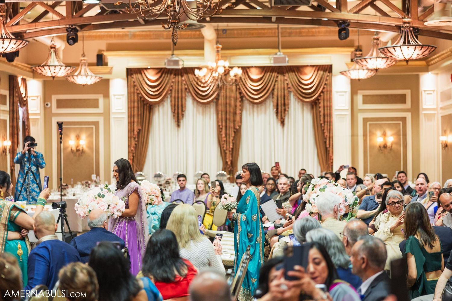 Celebration in an ornate ballroom with chandeliers and elegant draping as guests enjoy a cultural event.