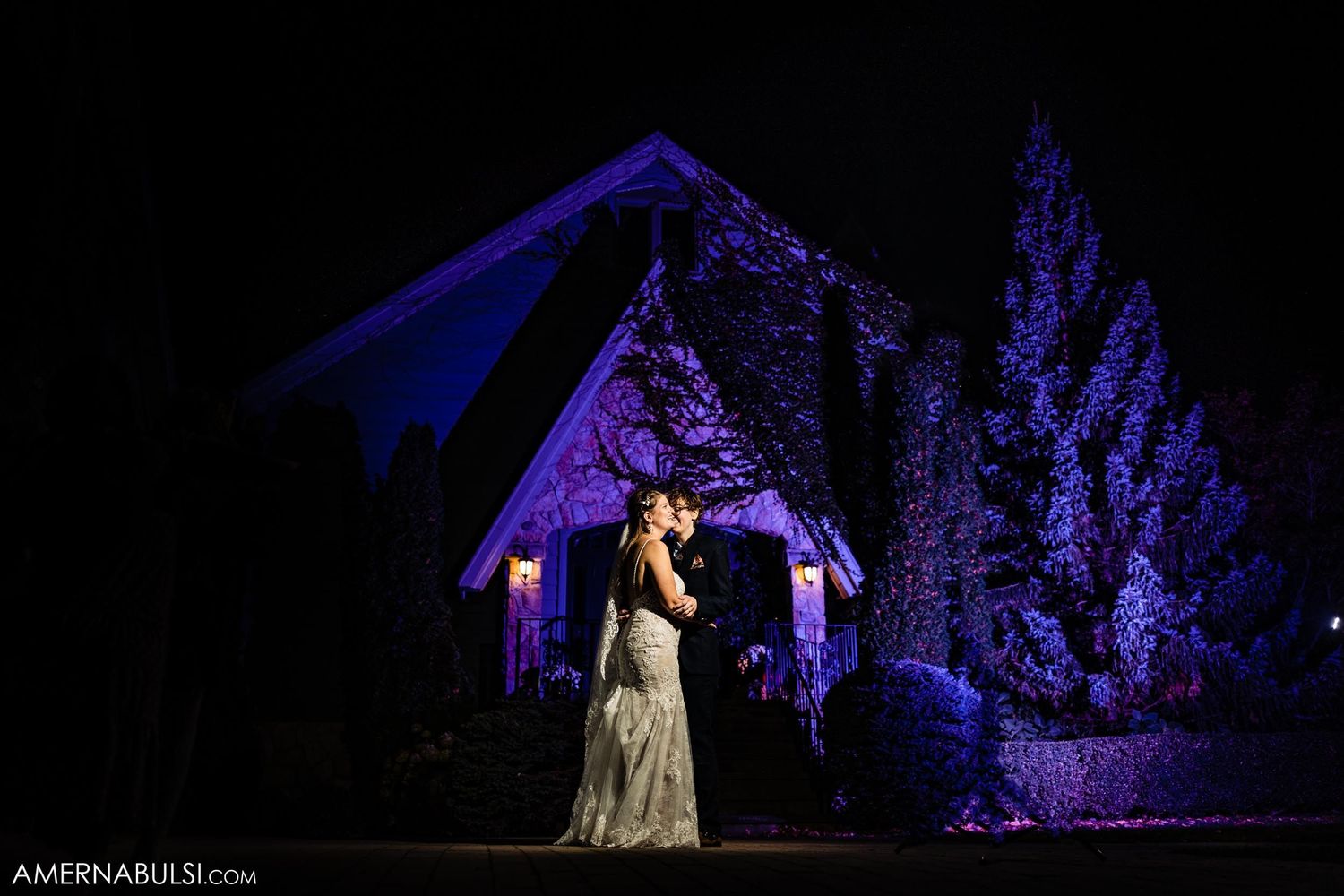 Wedding scene at night with purple lighting illuminating a gazebo and evergreen trees.