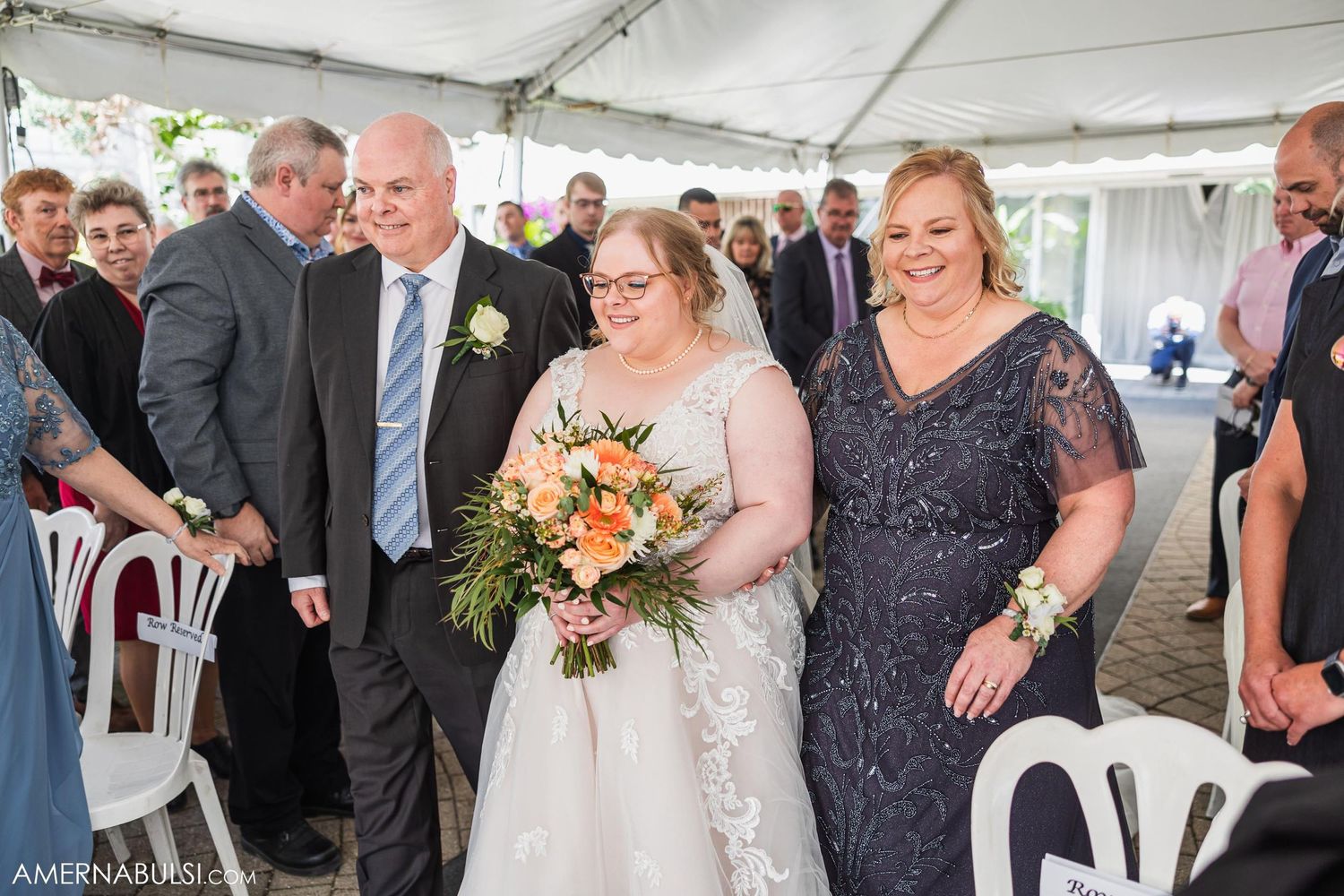 Wedding party members gathered under a white tent with peach floral arrangements.