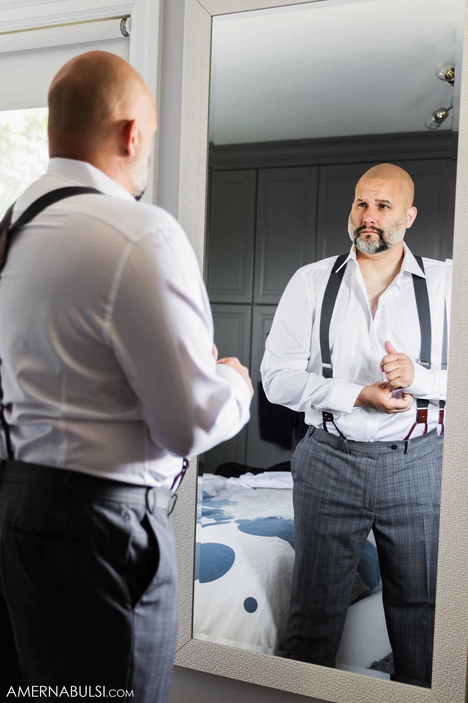 Person adjusting suspenders while looking in mirror during wedding preparation.