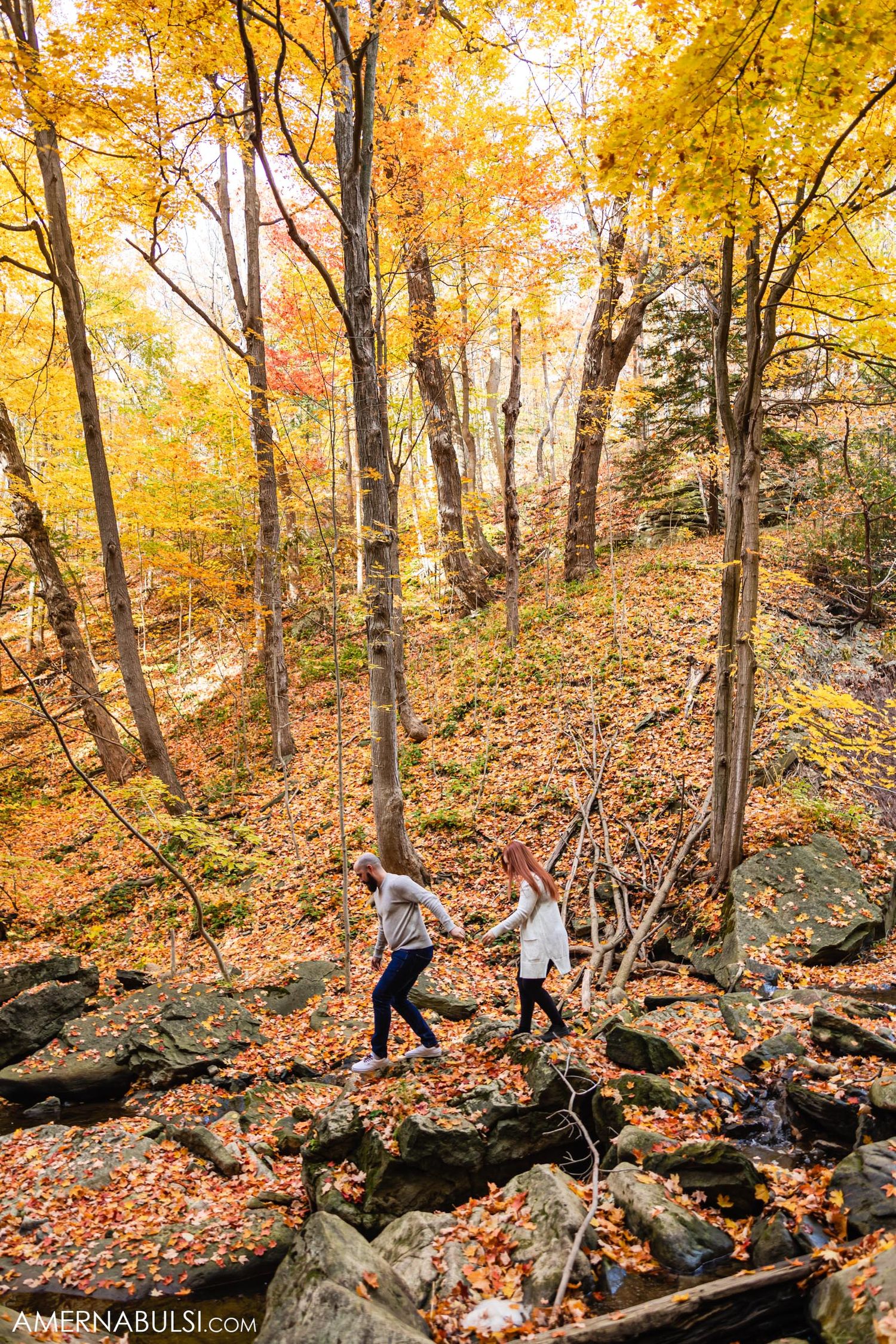 Couple walking through rocky forest terrain with golden fall leaves.