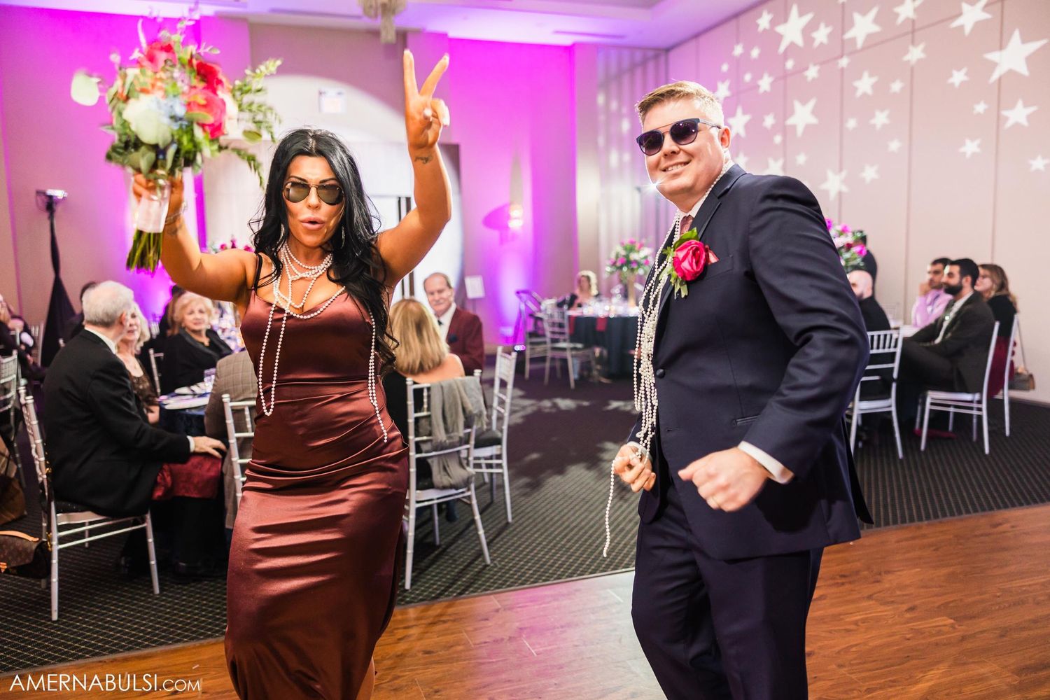 Wedding guests dancing energetically at reception with pink uplighting and elegant table settings.