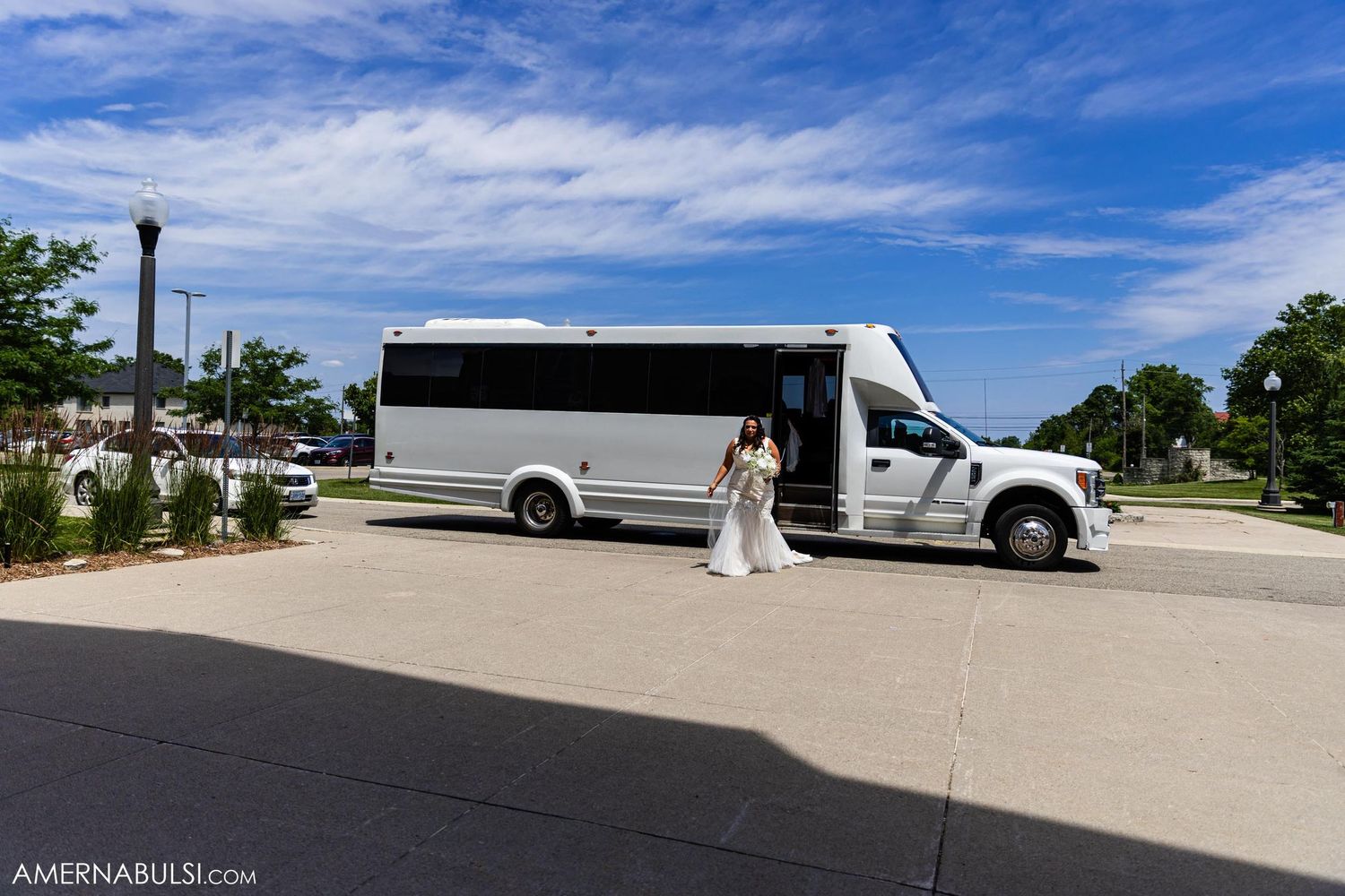 A white shuttle bus parked outside under blue skies during a wedding event.