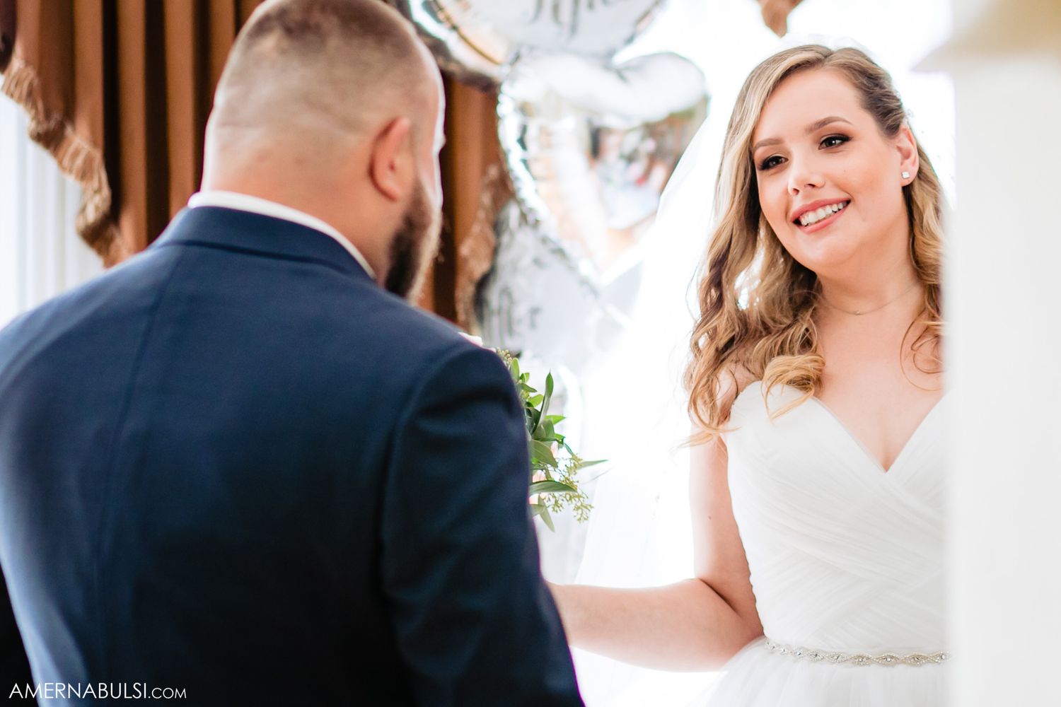 A couple shares a tender moment during their wedding ceremony in an elegant indoor setting.