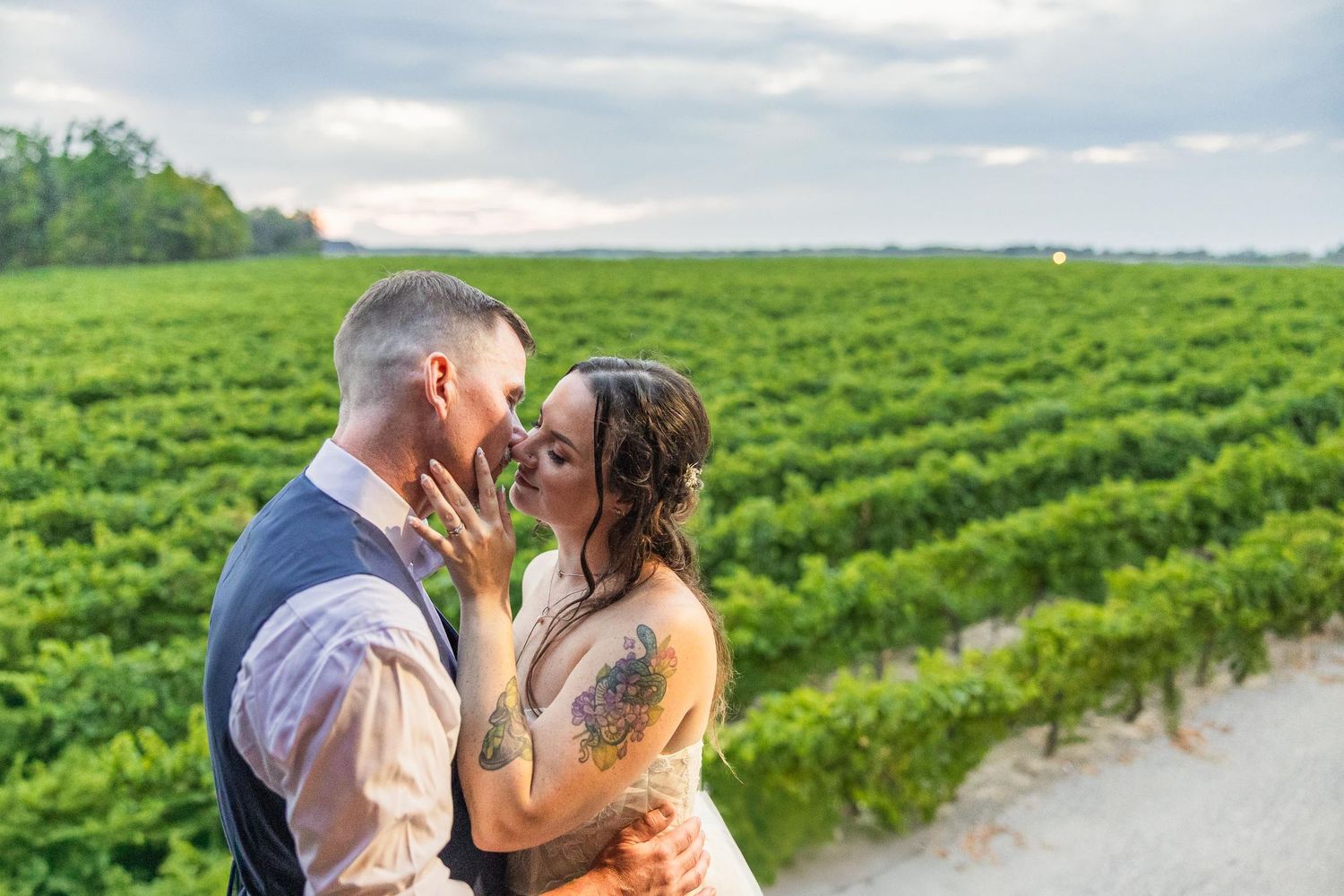 A romantic moment between a couple in a scenic vineyard with cloudy skies.