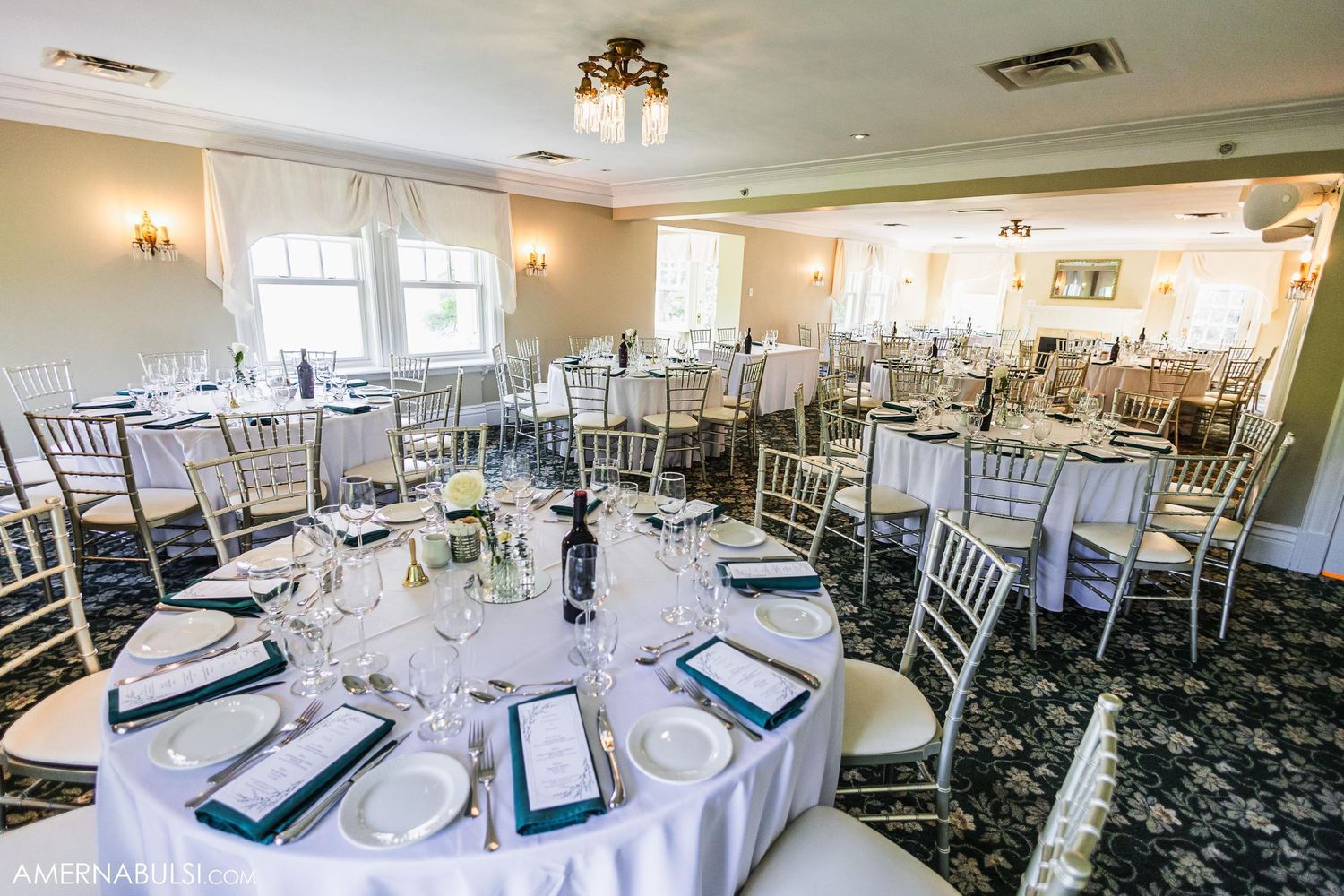 An elegant wedding reception room set with round tables, silver chiavari chairs and navy blue accents.