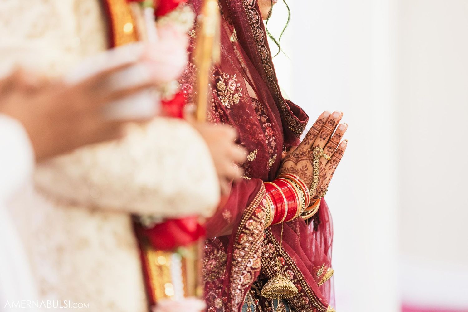 Close-up of hands with mehndi and traditional wedding jewelry during ceremony.