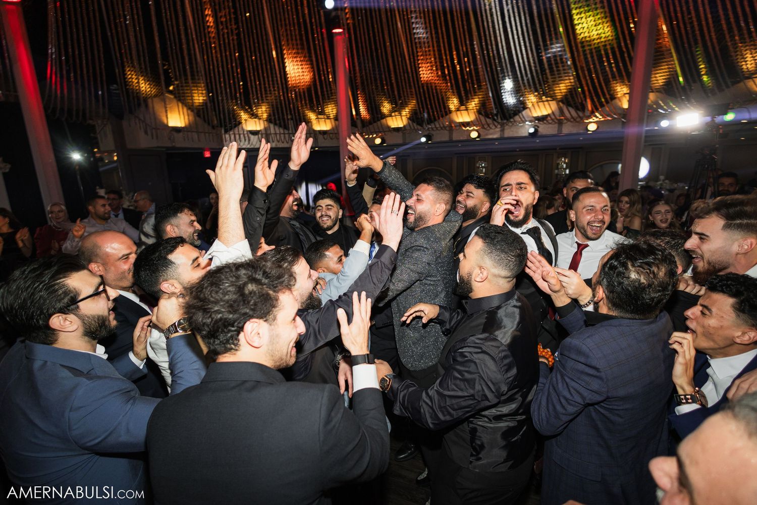 Concert crowd raises hands in excitement during a high-energy performance in a dark venue with stage lighting.