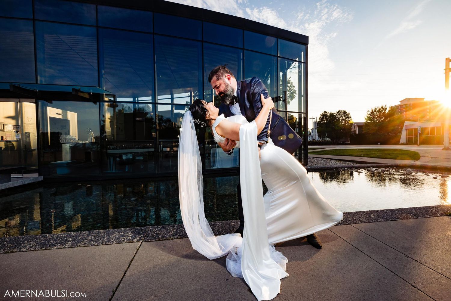 Romantic sunset dip pose at a modern glass building venue.
