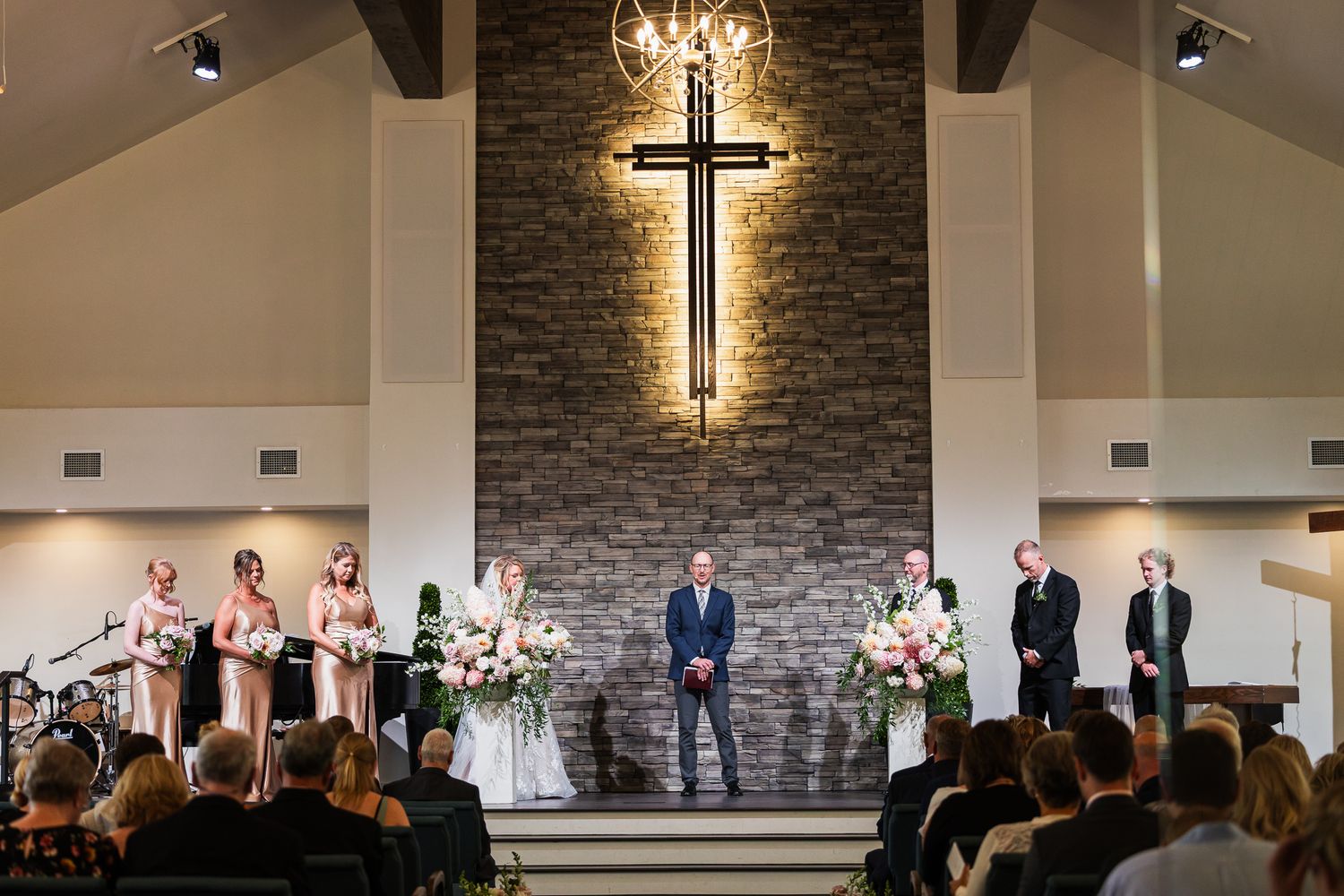 Modern church interior with illuminated cross on stone wall and wedding ceremony setup.