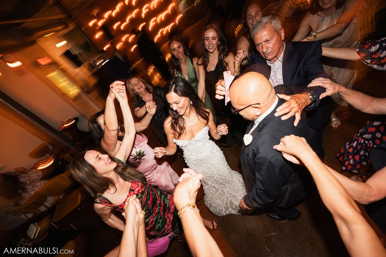 Wedding party members dance enthusiastically on a dimly lit dance floor.