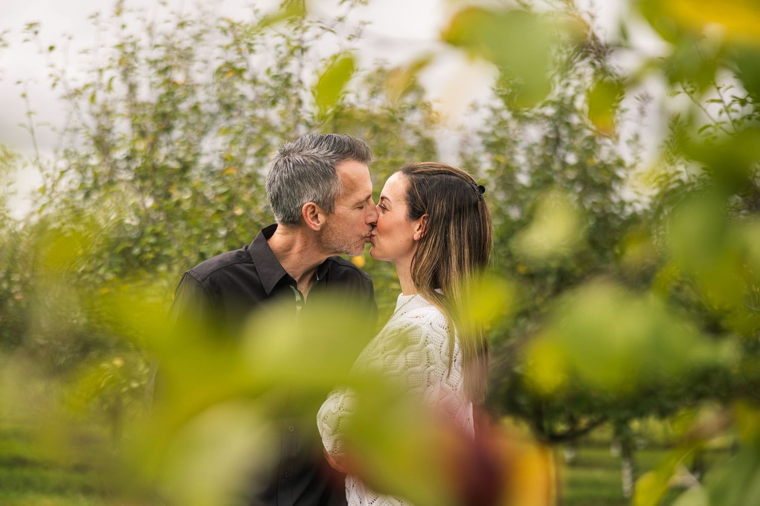 A couple shares a tender moment among blossoming trees in a garden setting.