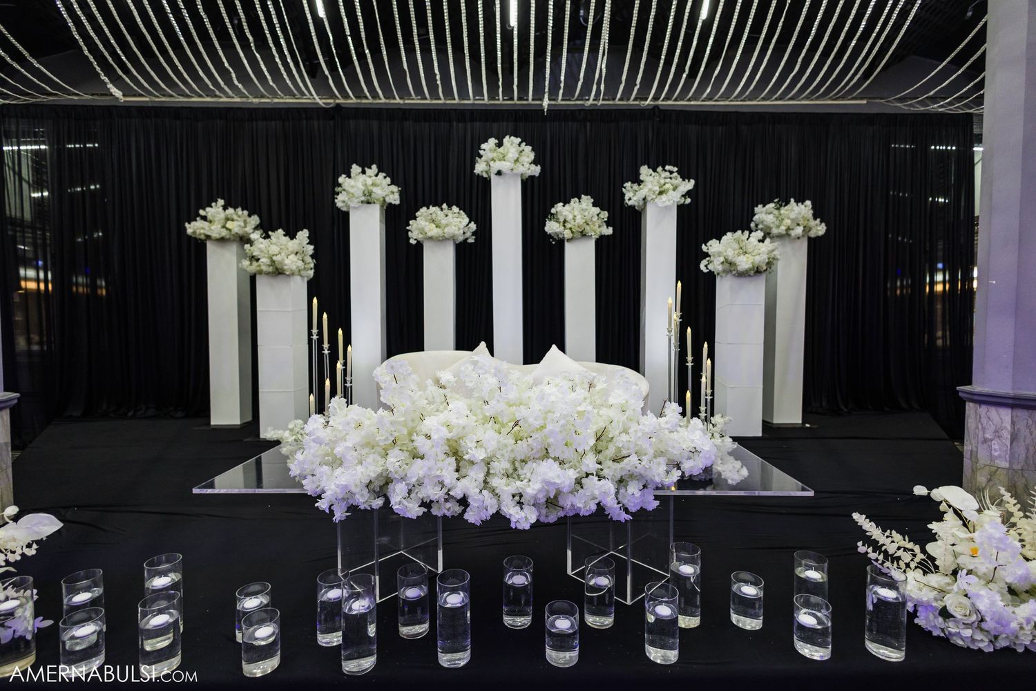 Elegant white floral centerpieces line a dark reception hall with dramatic lighting and modern decor.