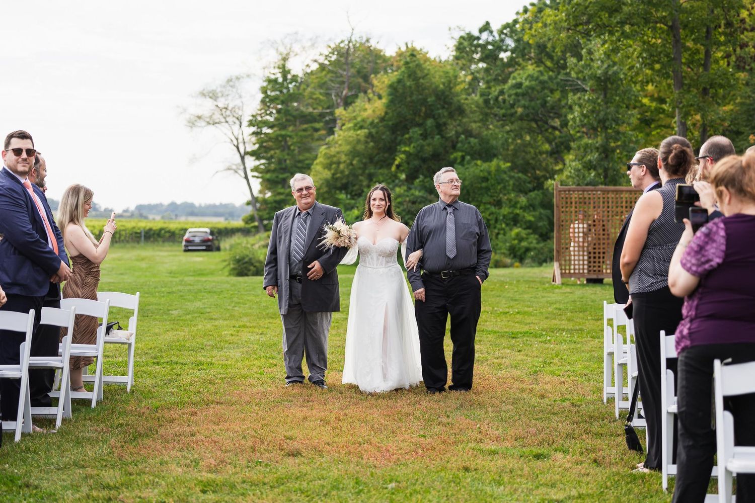 Outdoor wedding ceremony setup with guests seated in white chairs on a grassy lawn.