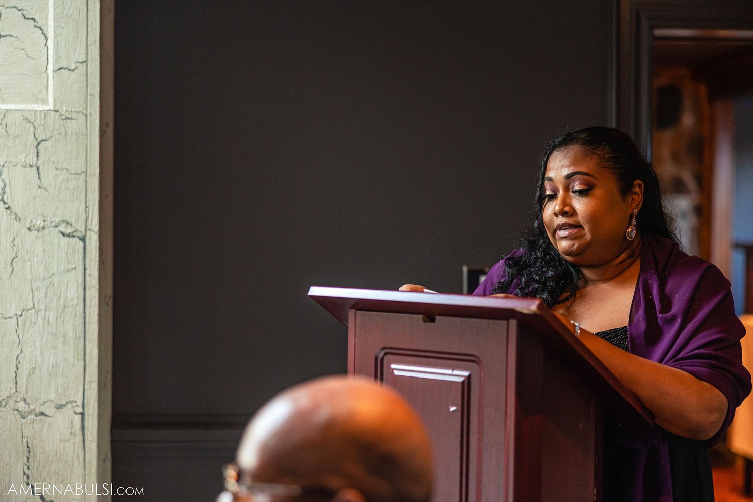 Event speaker at wooden podium during formal celebration.