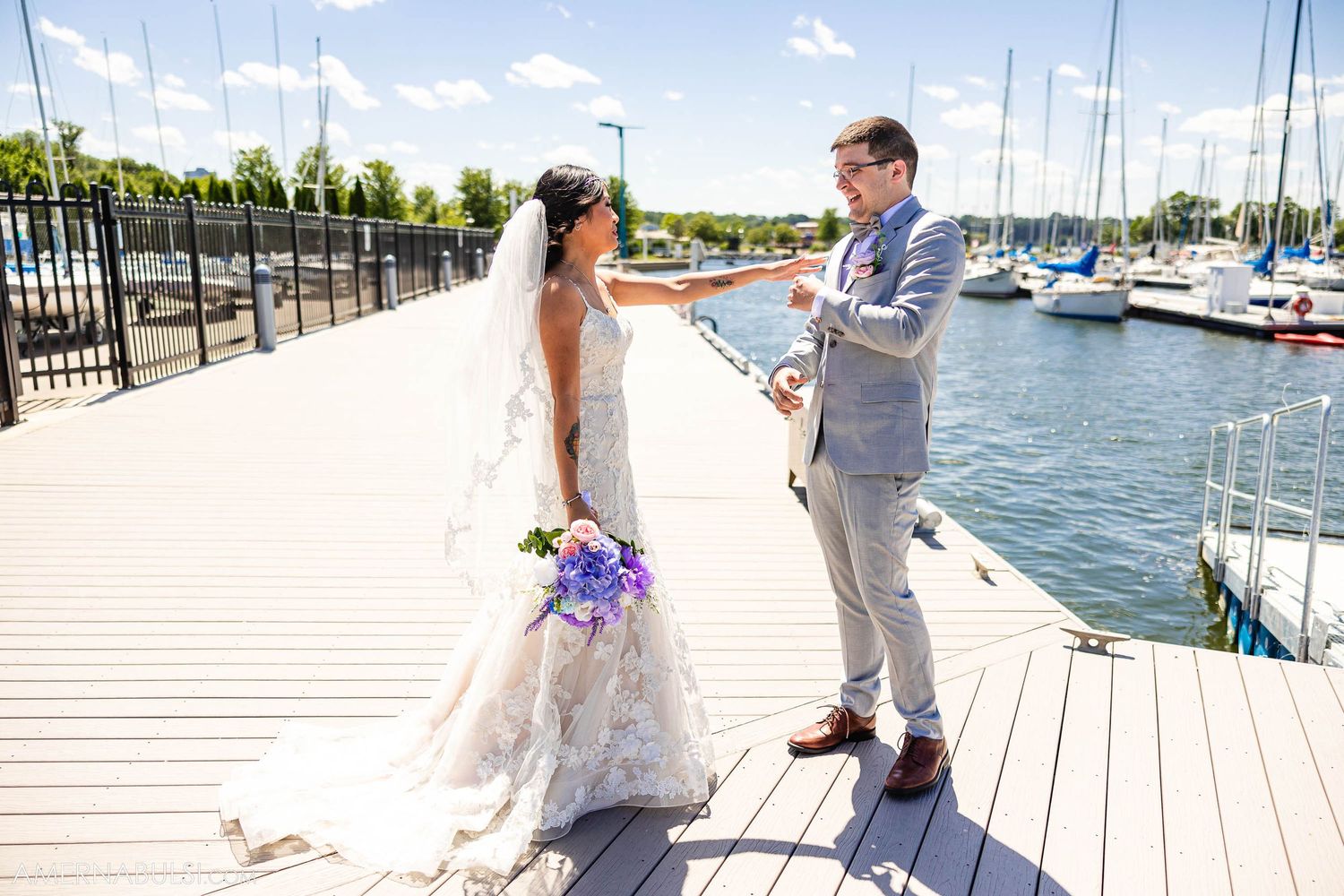 A couple reads their vows on a wooden dock with boats and water in the background.