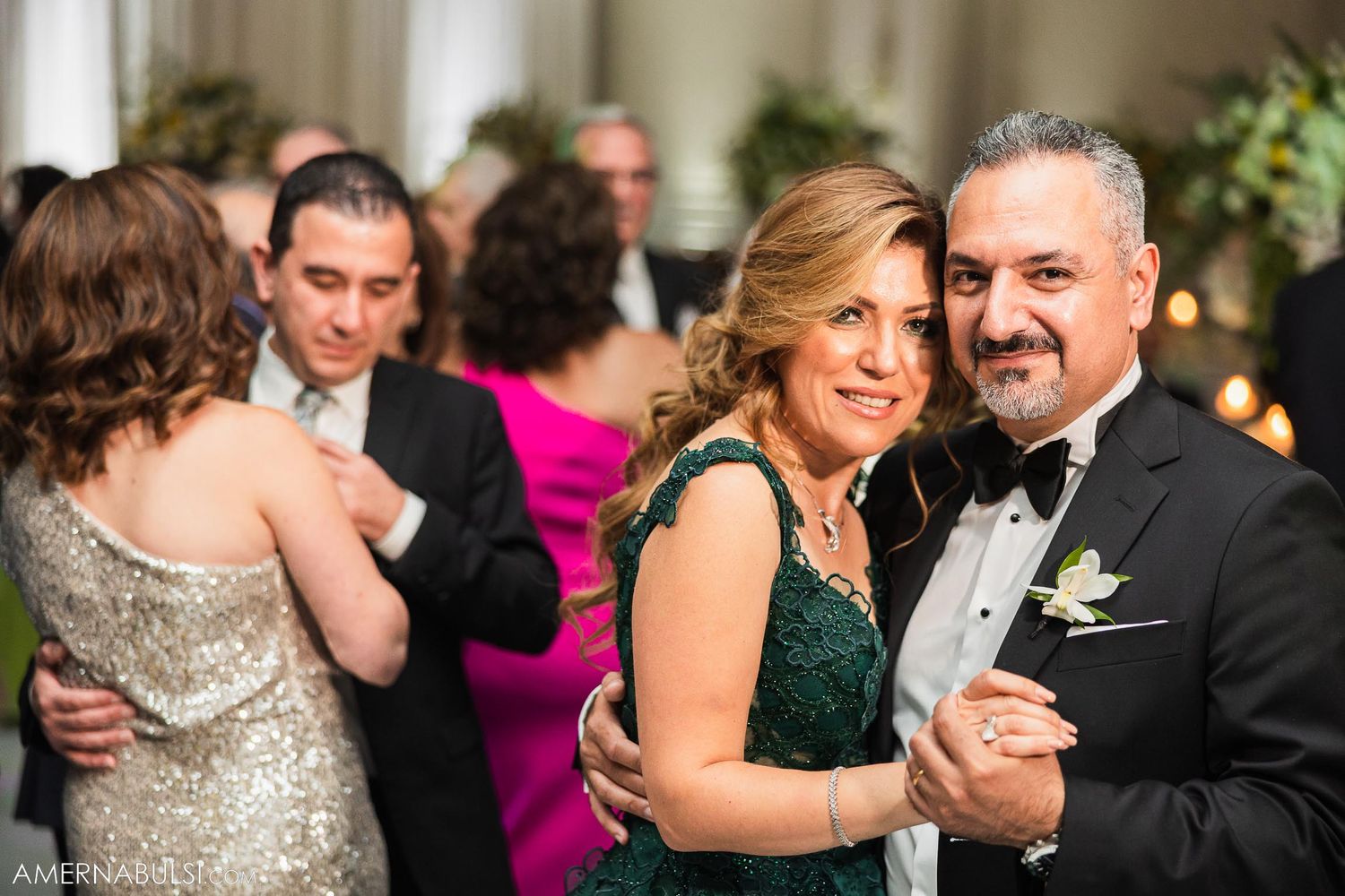 Formal wedding reception guests dancing and celebrating in black tie attire.