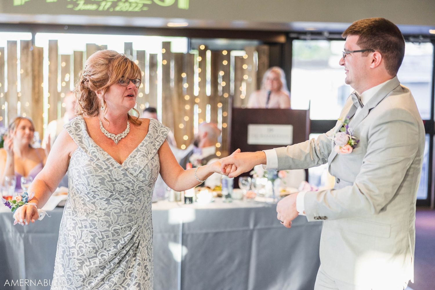 Wedding couple dances joyfully at reception with decorated tables in background.