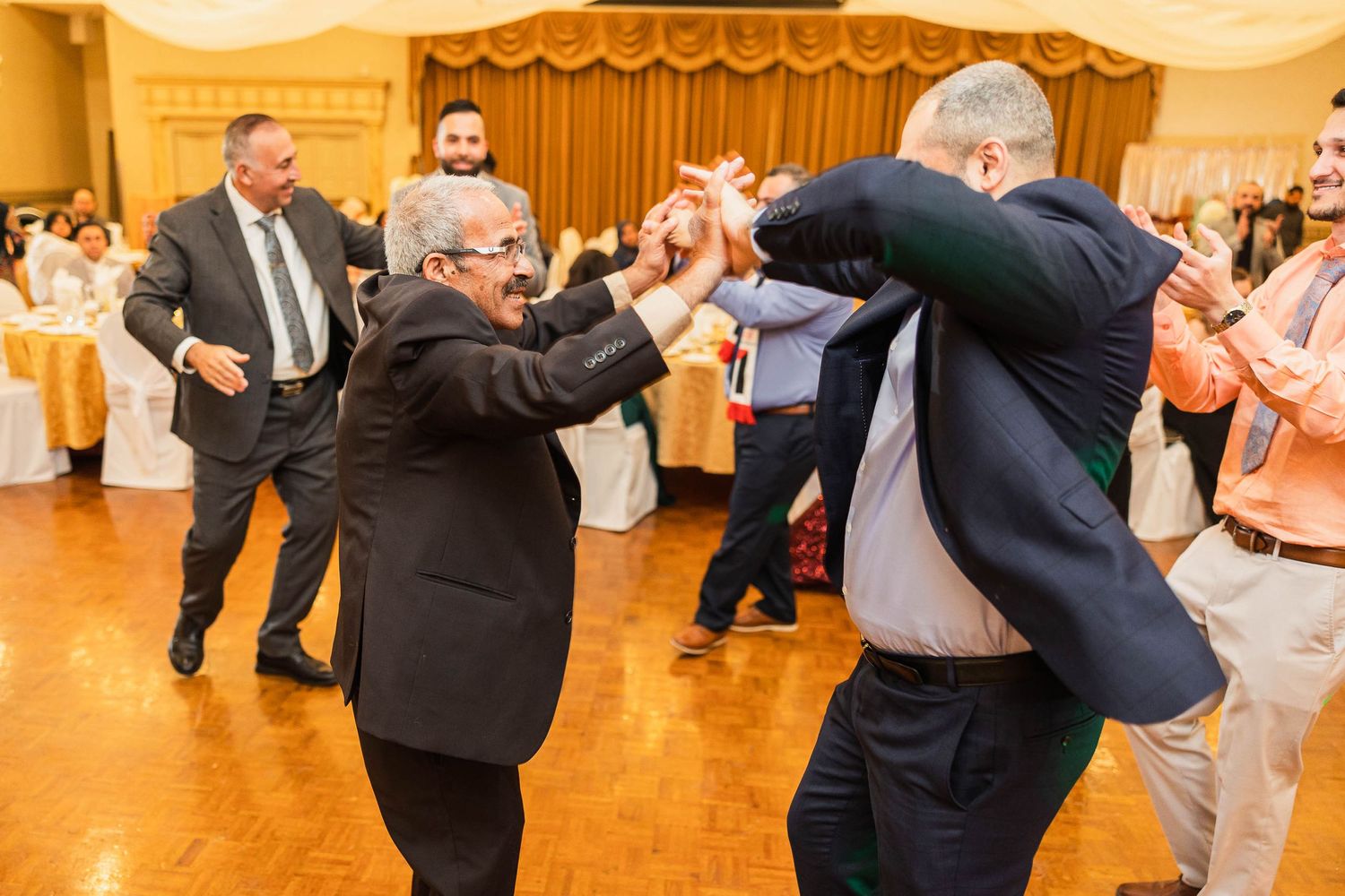 Guests enjoying enthusiastic dancing at a wedding reception on a wooden dance floor.