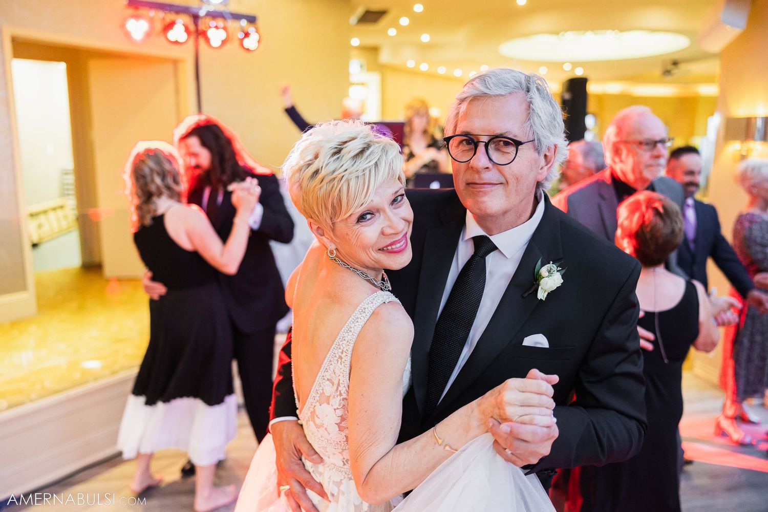 A couple shares a dance at their wedding reception under warm lighting.