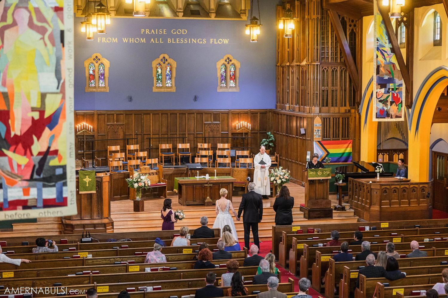 View of church interior with wooden pews and stained glass windows during ceremony.