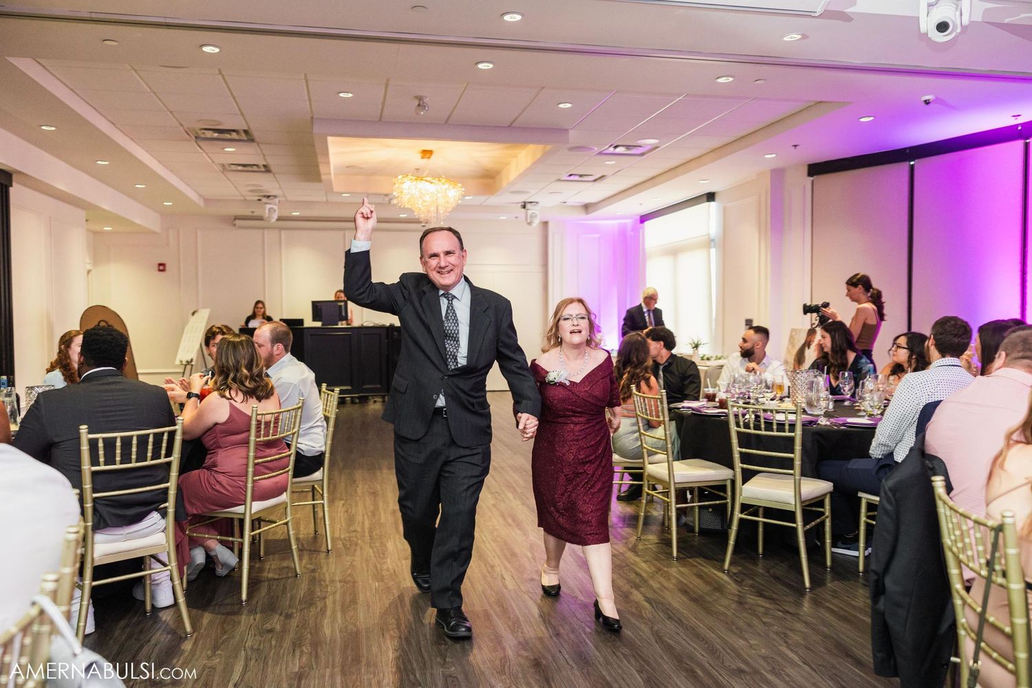 Wedding party members walk down the aisle at reception with arms raised in celebration.