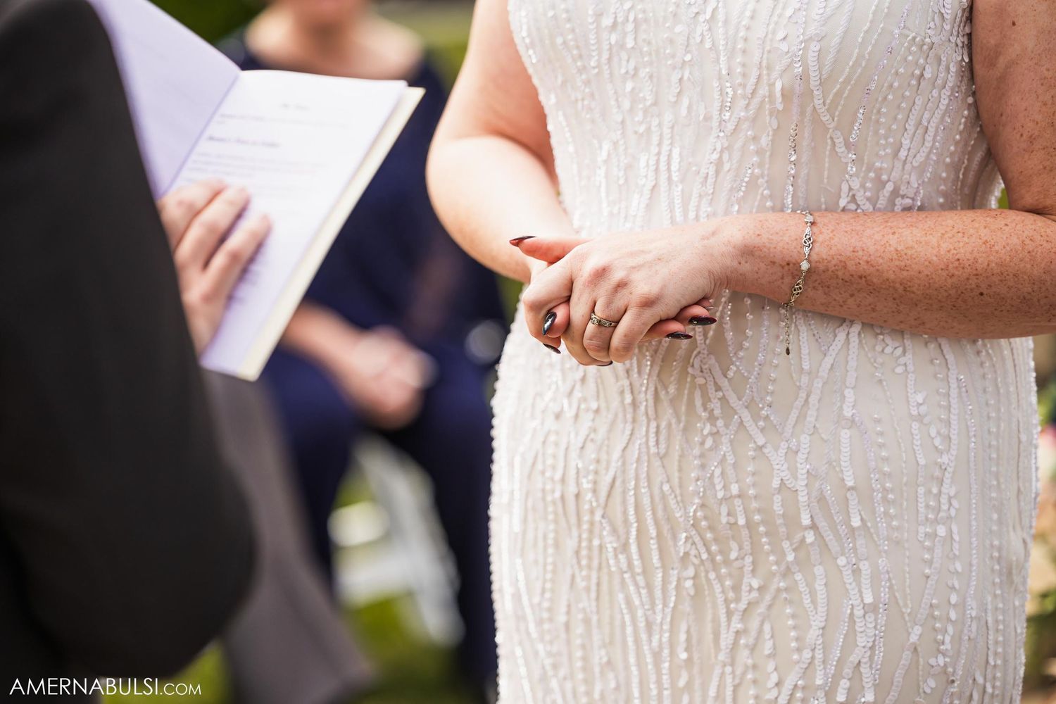 Close-up detail of a bride in a beaded white dress during an outdoor wedding ceremony.