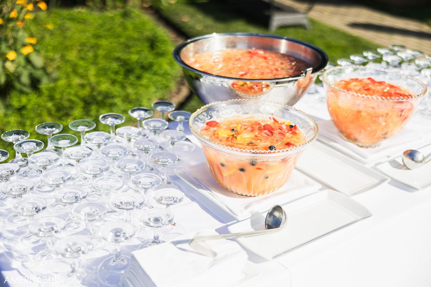 Pink cocktails in glass bowls displayed on white table with ice at outdoor event.