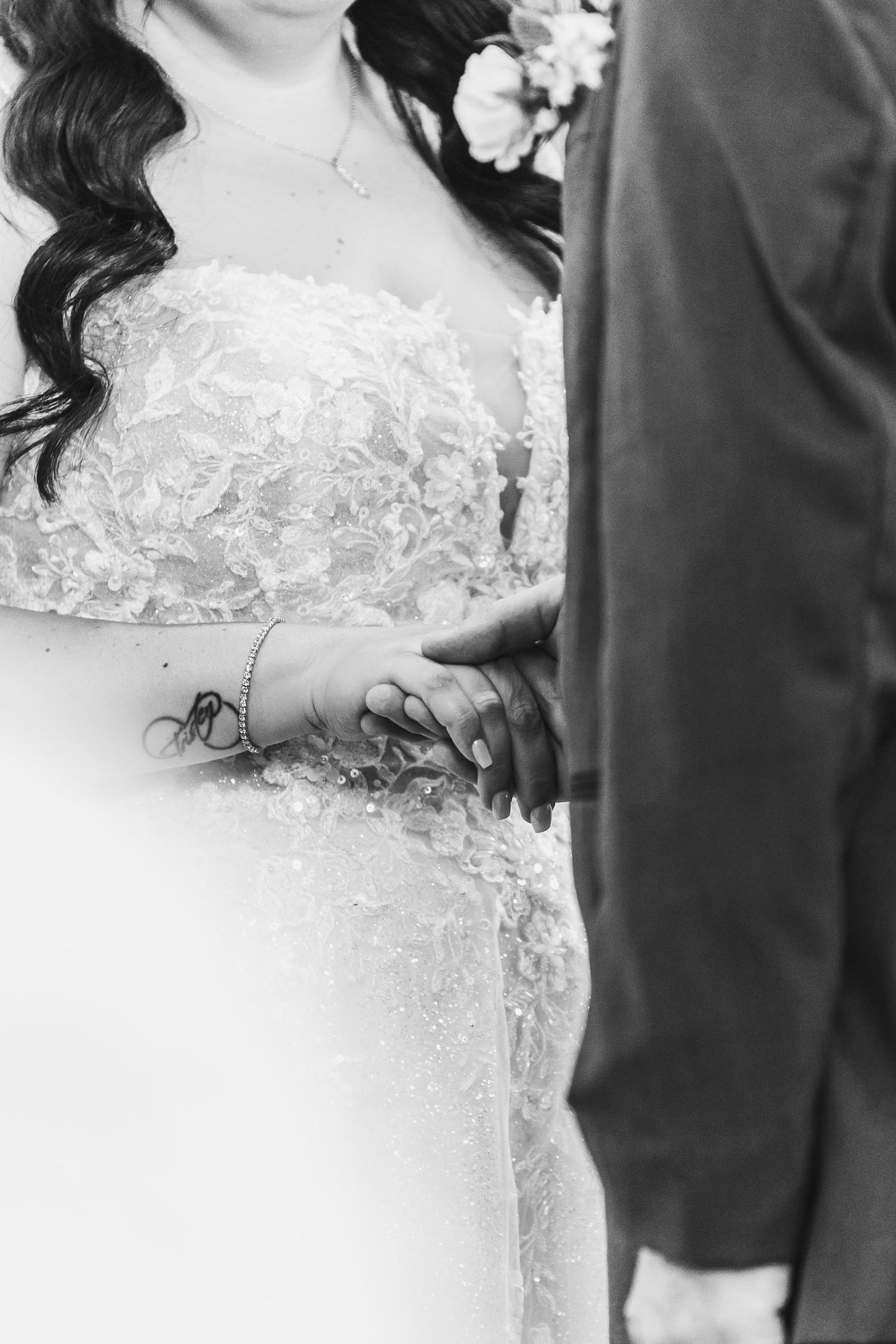 Close-up detail of lace wedding dress and clasped hands during a wedding ceremony.