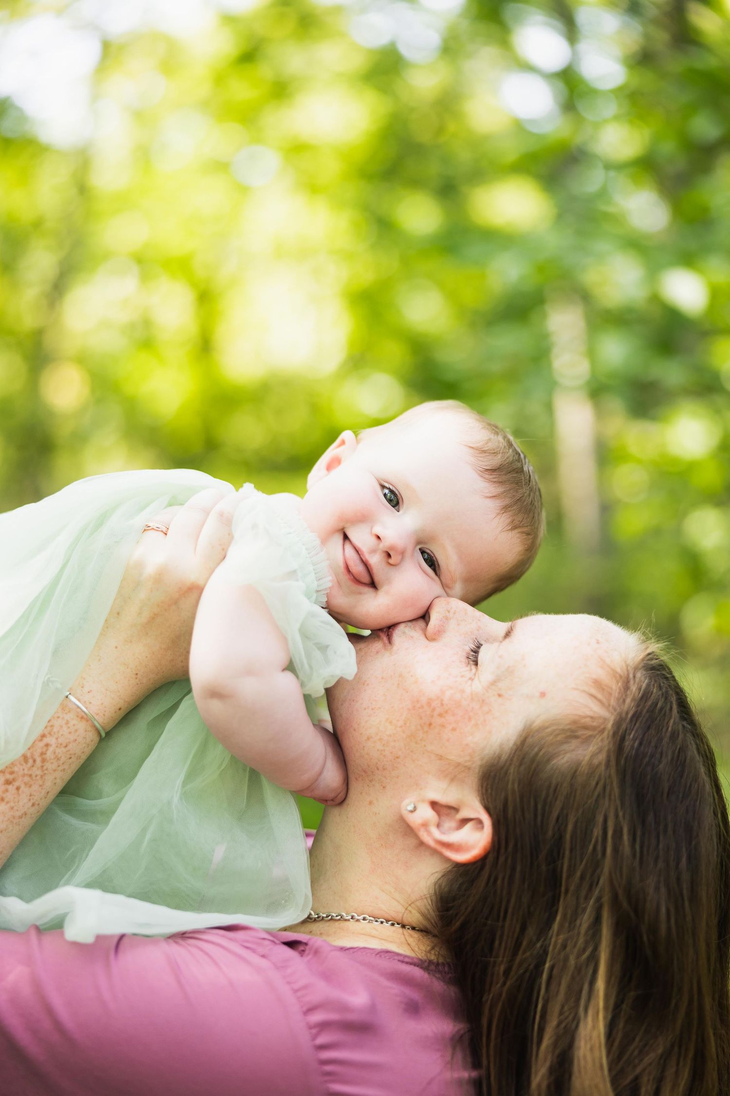 Sweet moment between parent and baby in matching mint green outfits against sunny forest backdrop.