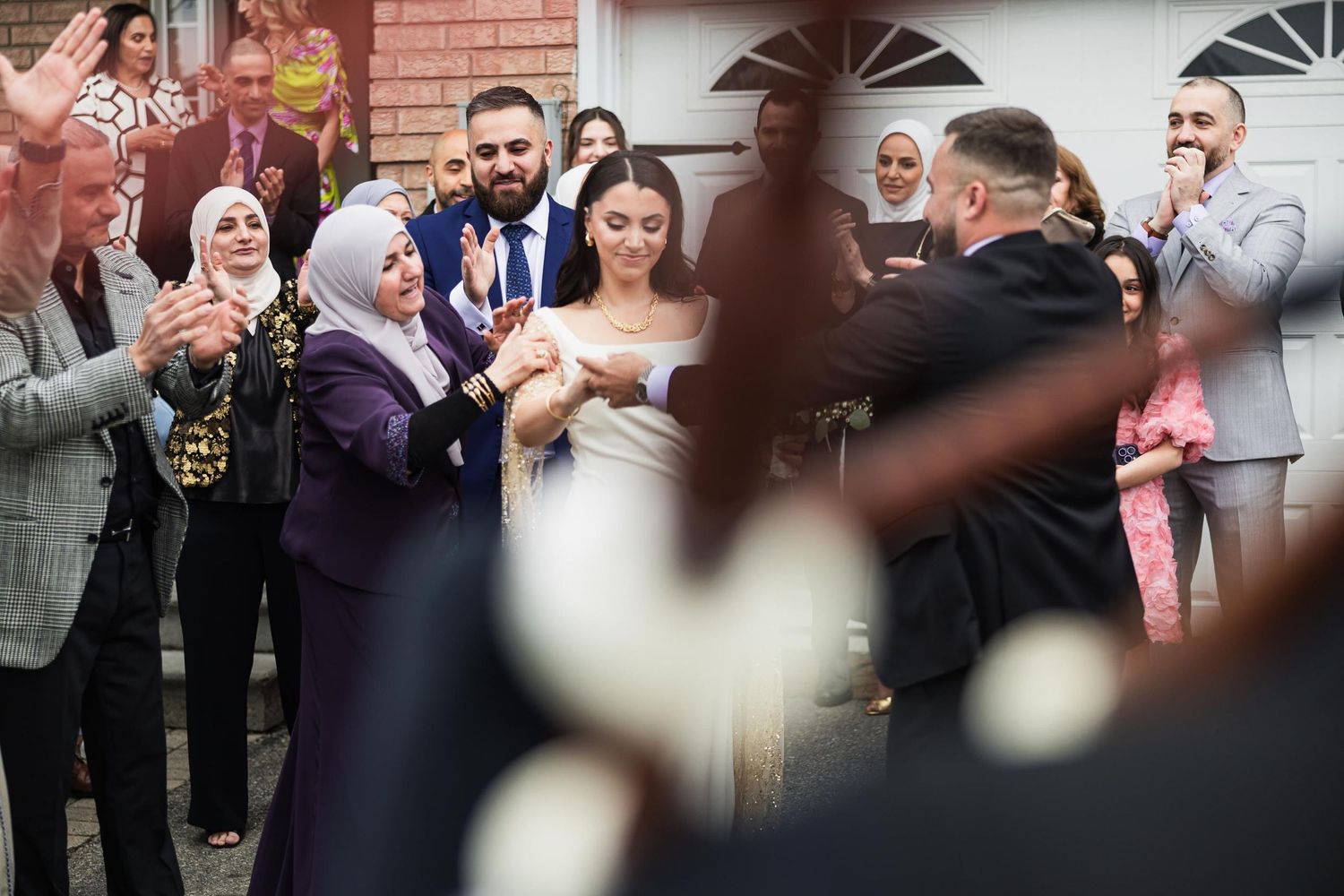 Wedding guests celebrate during a traditional ceremony outside a brick house.