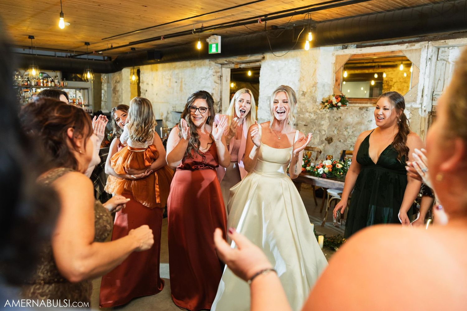 A bride in a white gown celebrates with bridesmaids in burgundy dresses at a wedding reception.