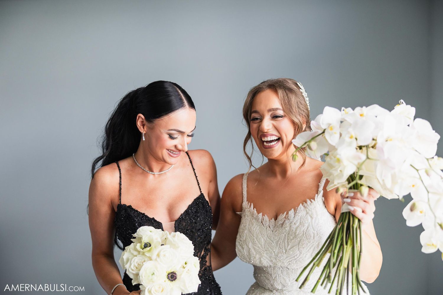 Joyful wedding moment with bride holding white orchid bouquet alongside bridesmaid.