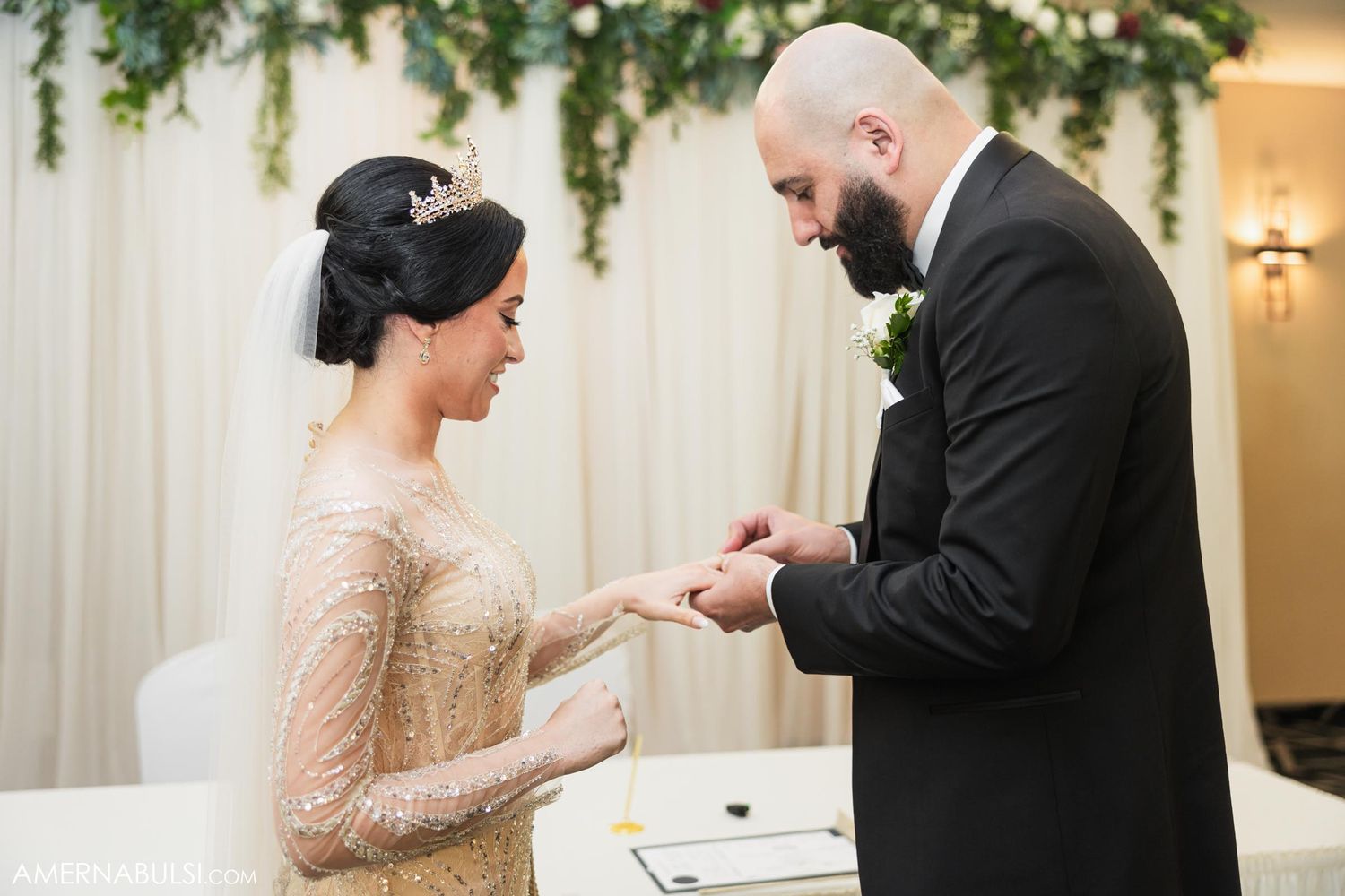 Couple exchanging rings during wedding ceremony under floral arch.