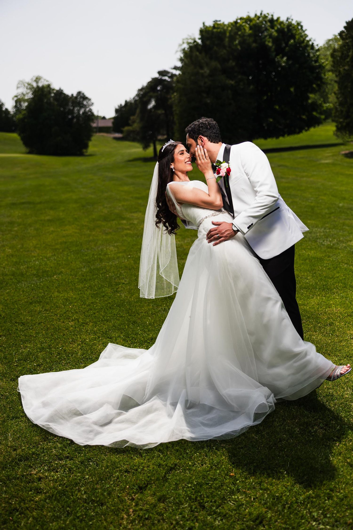 Bride and groom share romantic kiss on manicured green lawn during outdoor wedding.