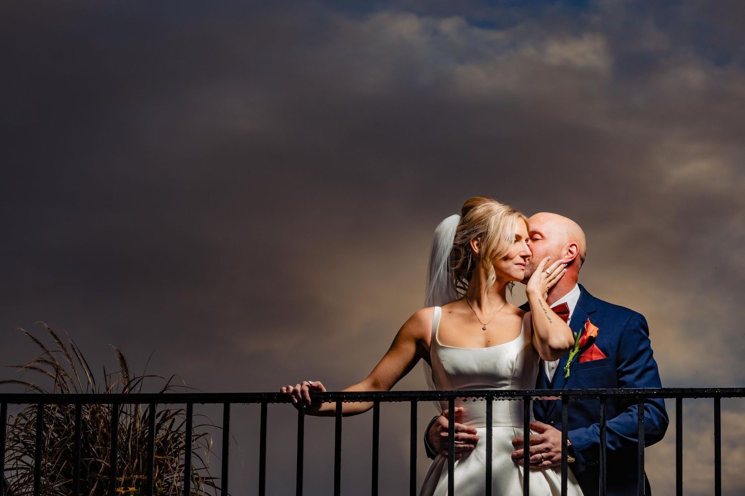 Dramatic silhouette of wedding couple against stormy sky at sunset.