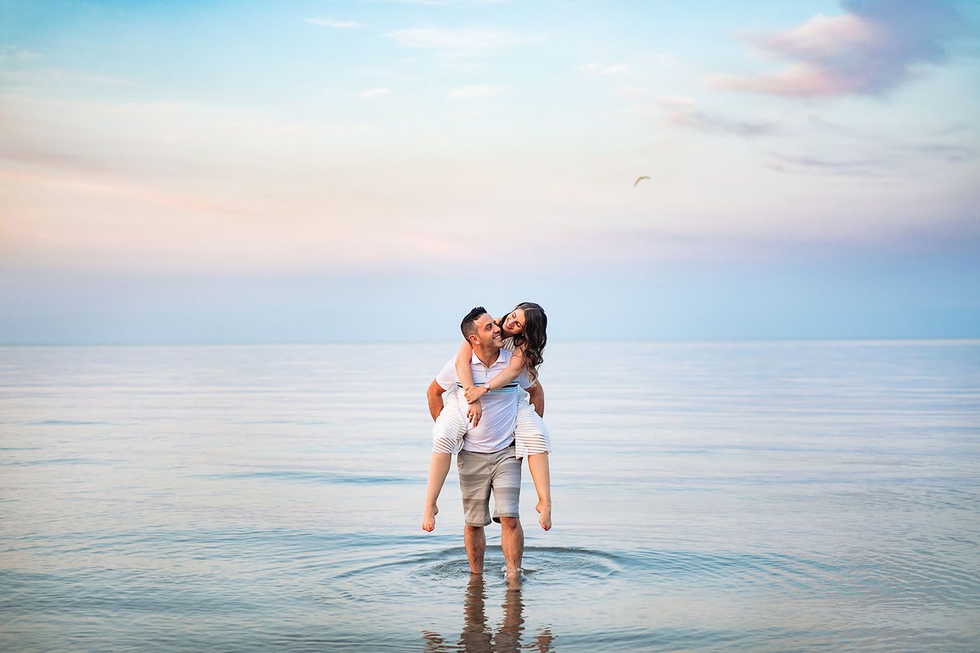 Couple wading in calm ocean waters during a pastel sunset.