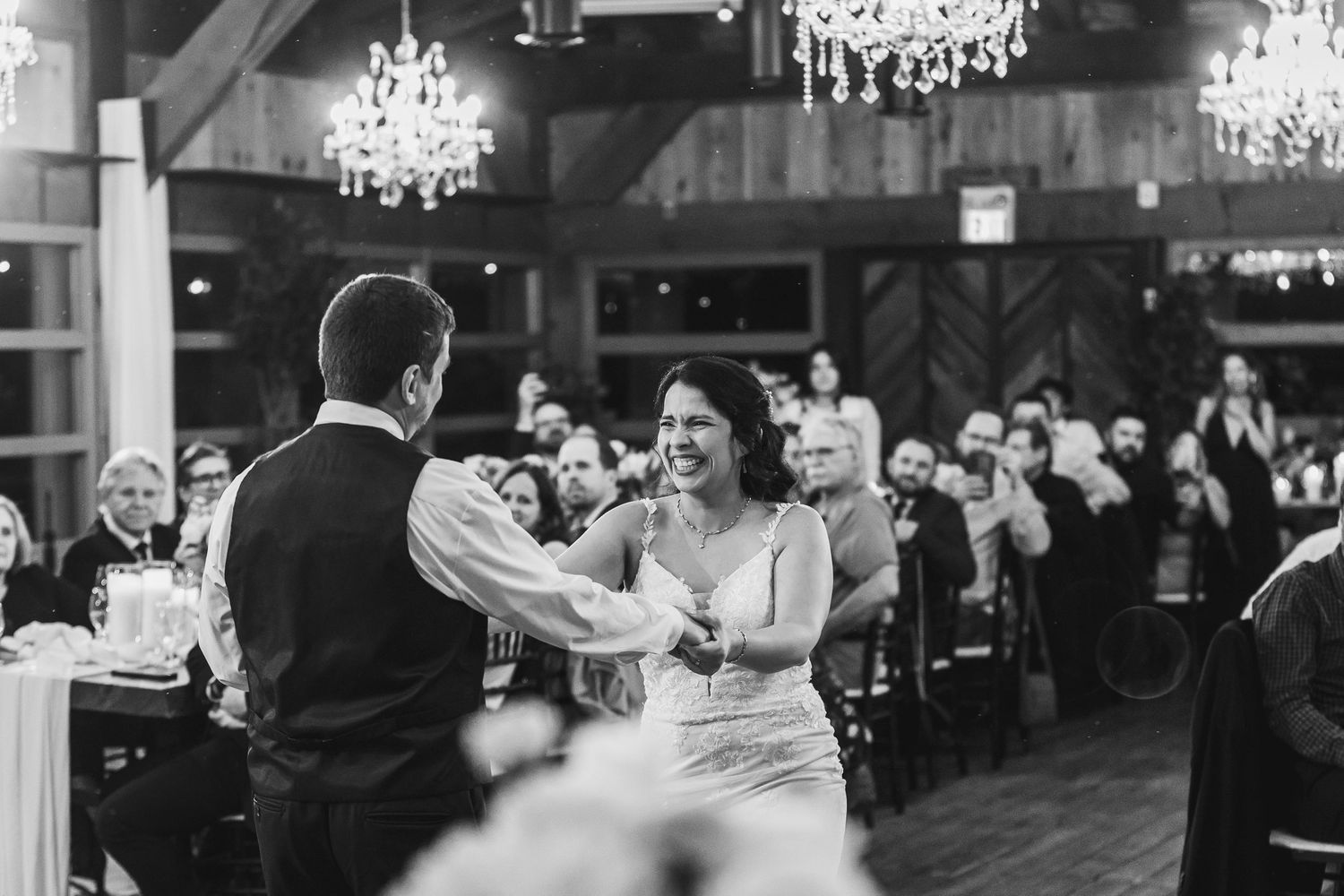 Black and white photo of a bride and groom sharing their first dance at a wedding reception with chandeliers above.