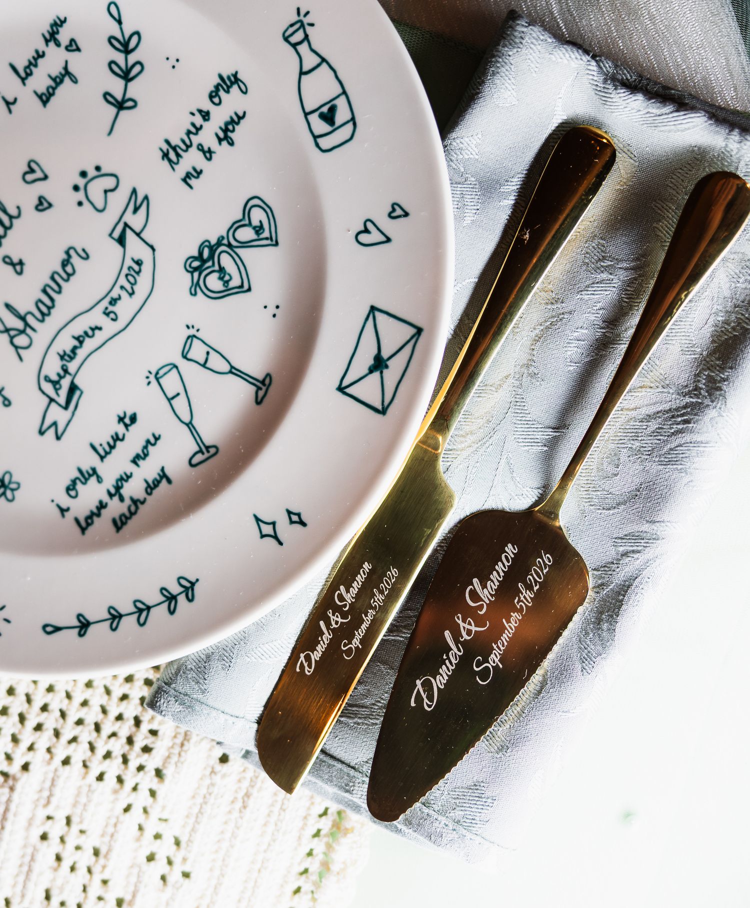 Custom engraved gold cake server set beside a personalized illustrated wedding plate with romantic doodles.