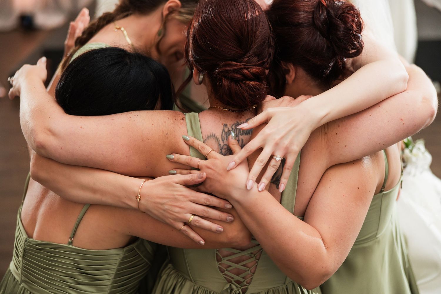 Bridesmaids in sage green dresses share a warm group hug, showing unity and friendship on a wedding day.