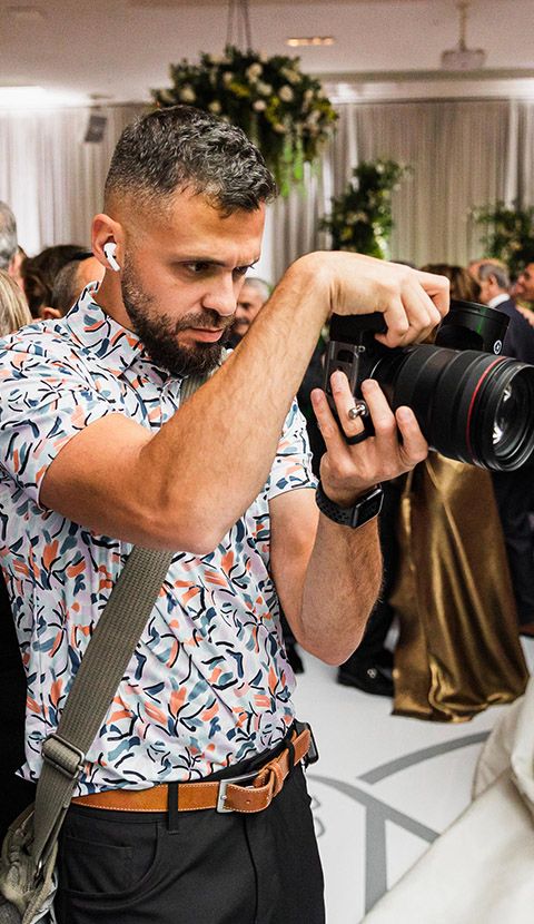 Professional photographer wearing a floral shirt demonstrates different camera angles and shooting positions.