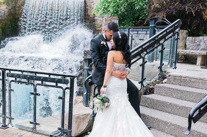 Wedding portraits by cascading water feature with white dress contrasting against dark surroundings.