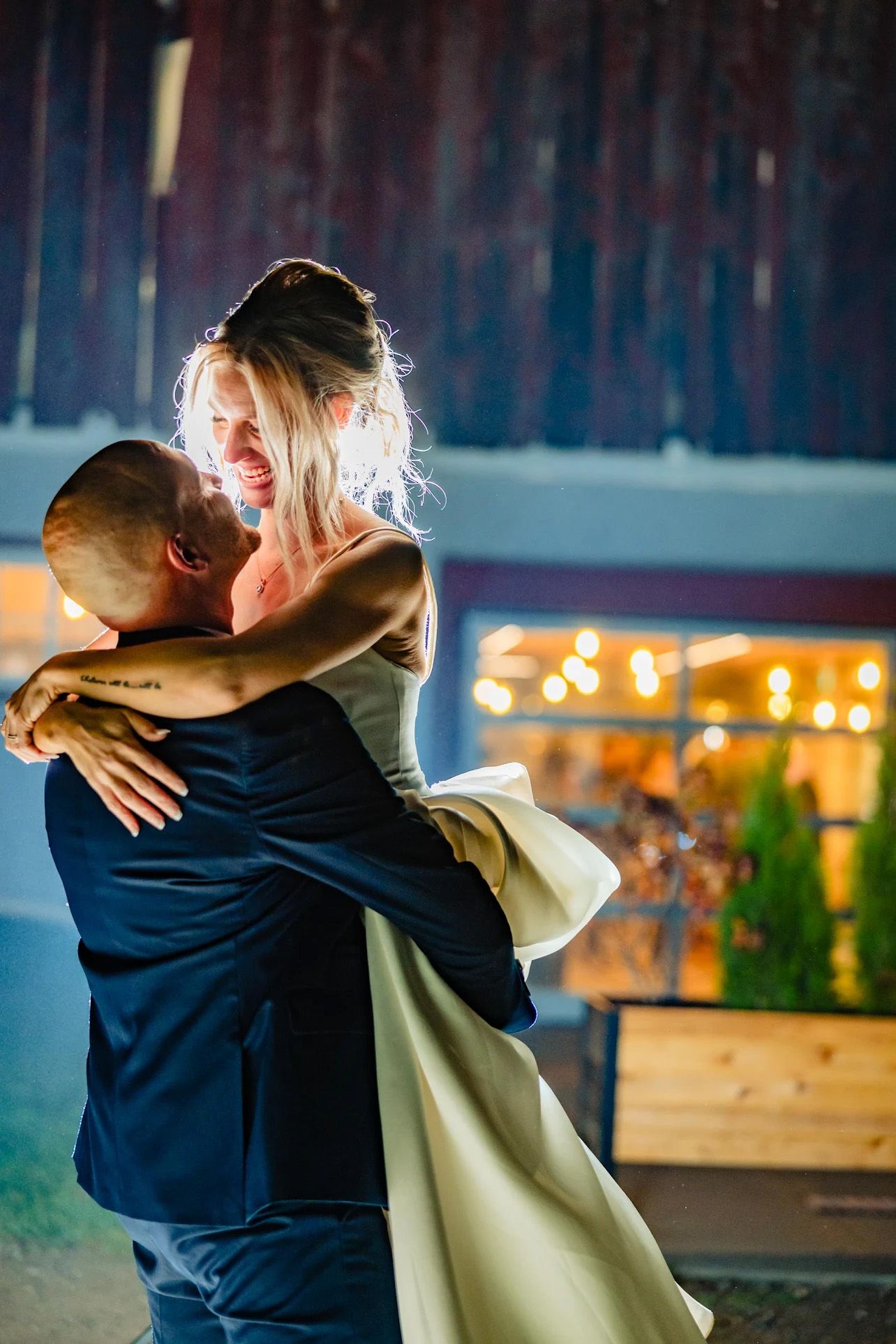 Romantic couple embracing at dusk with glowing lights in the background creating an intimate atmosphere.